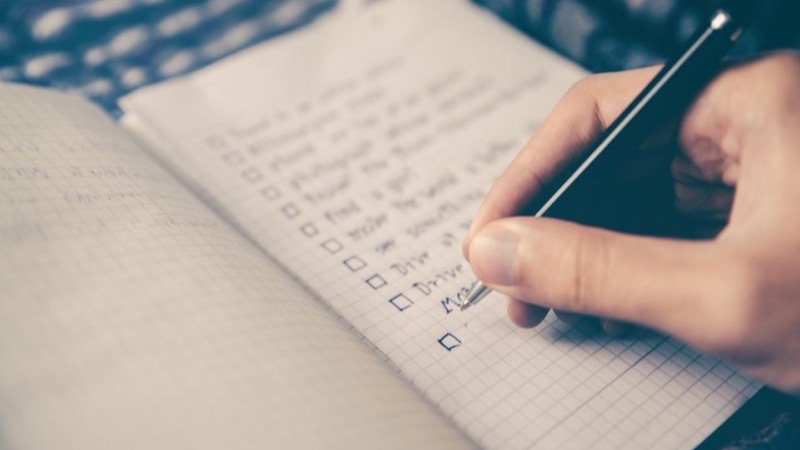 An open notebook with a handwritten checklist on a clean desk beside a pen